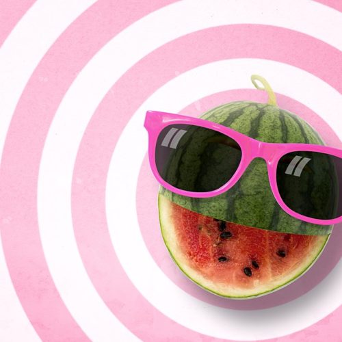 Watermelon with a cut for a smile wearing sunglasses on a background made of alternating pink and white concentric circles