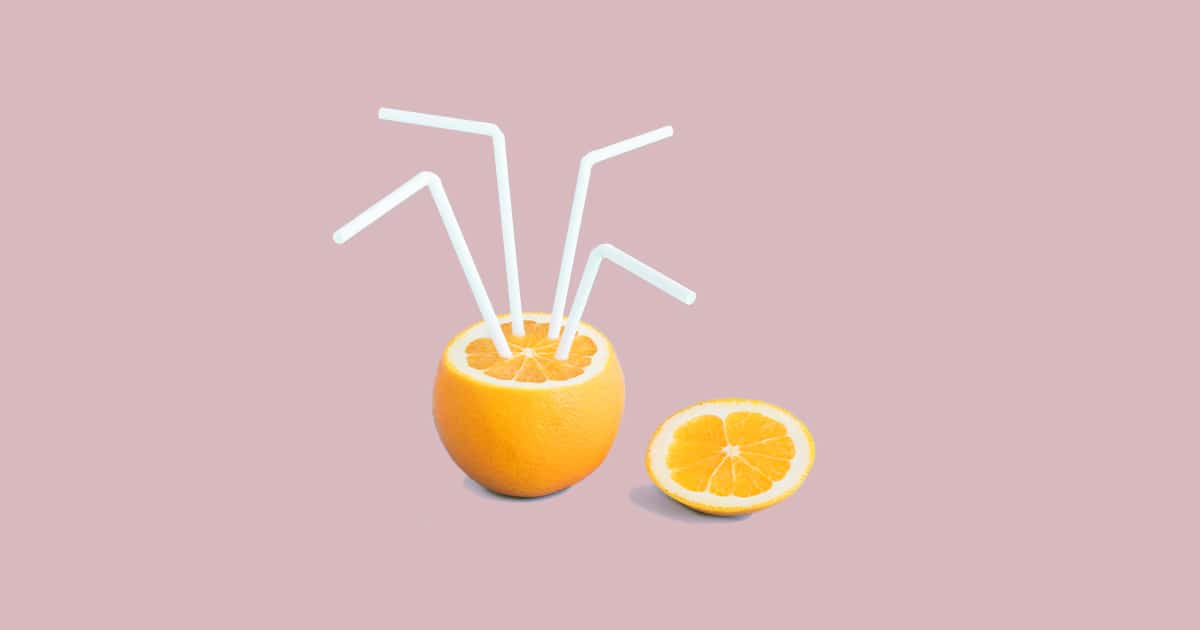A cut orange with four straws sticking out like a drink on a pink Juiced Rite brand color background