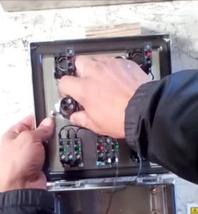 Hands Loosening the Lock Nut on the Backside of the Button on the inside of a control panel for a Juiced Rite Machine