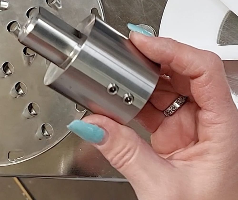 A hand holding a blade holder hub for a cold press juice machine.
