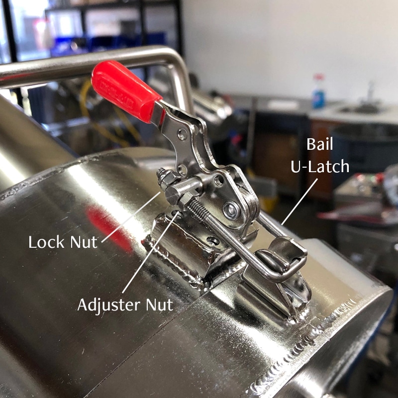 Close up of the bail latch at the top of the juice machine that holds the chute in place. There are labels and lines indicating the parts of the bail latch.