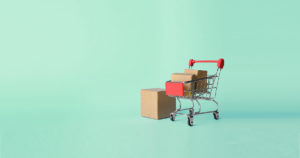 Mini shopping cart with boxes inside and beside it on a light green background.