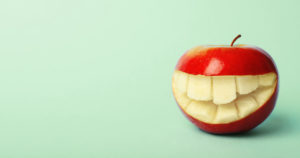 Apple with a carved toothy grin on a green background.
