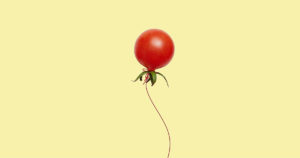 Red cherry tomato with a string to look like a floating balloon on a yellow background.