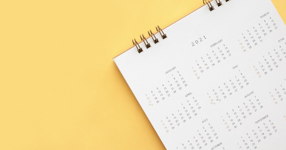 Coil bound calendar with many months on white paper laid on a yellow background