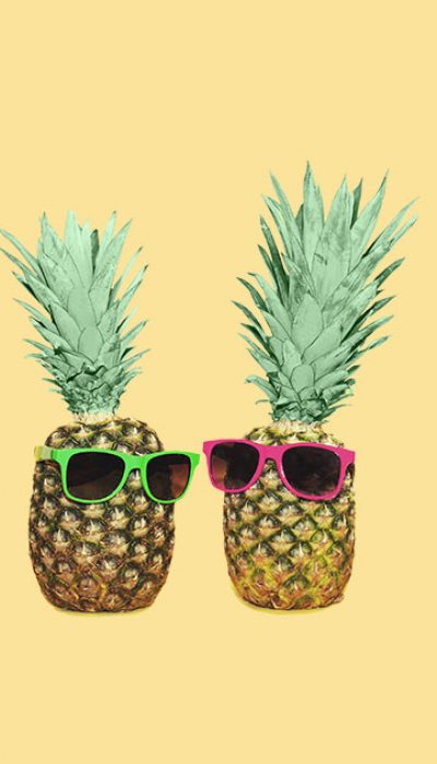 Two pineapples wearing sunglasses on a yellow background